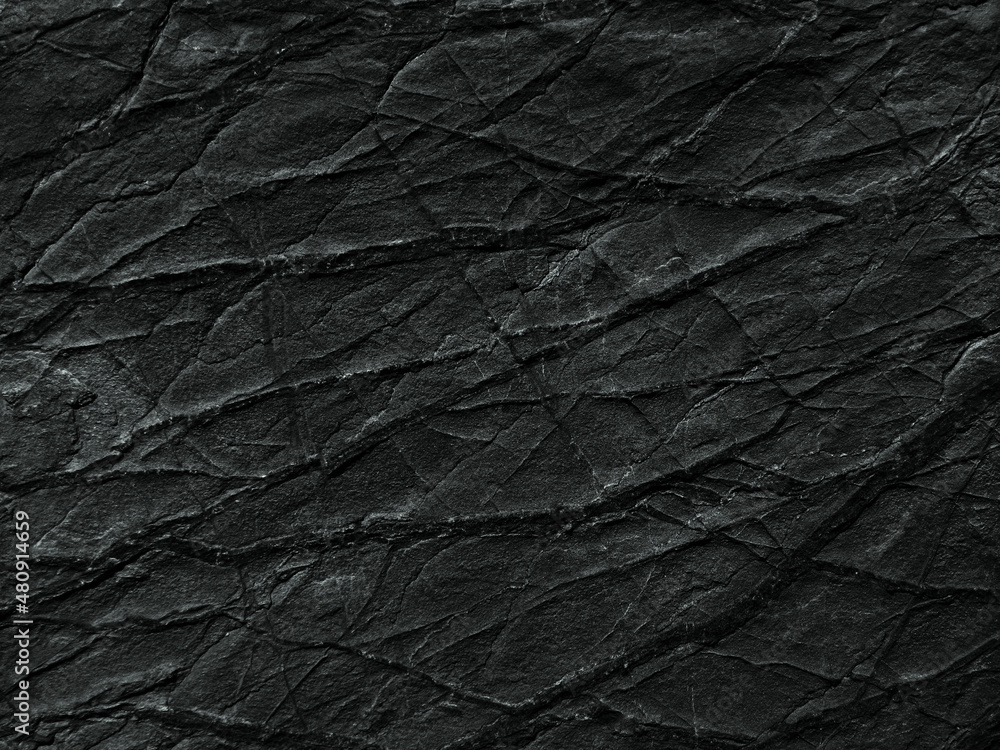 Black rock texture with cracks and veins. Closeup. Dark rough stone