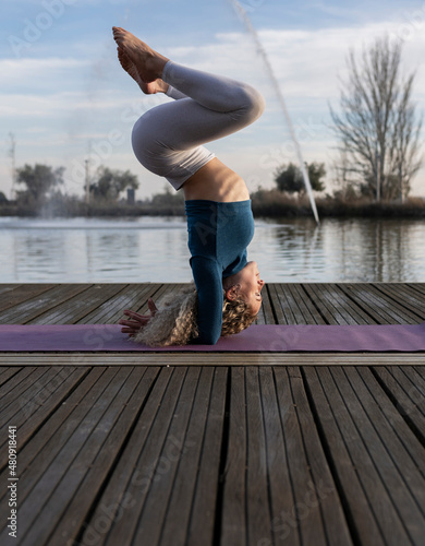 blonde curly hair woman, does a handstand on a pier yoga posture. photo