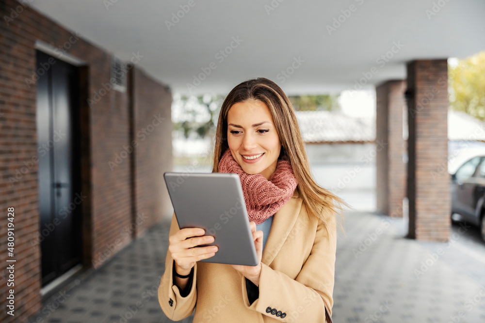 A businesswoman with a tablet outdoors. A happy businesswoman in warm clothes standing outdoors and using the tablet for web research. A businesswoman with a tablet outdoors. A happy businesswoman in warm clothes standing outdoors and using the tablet for web research.