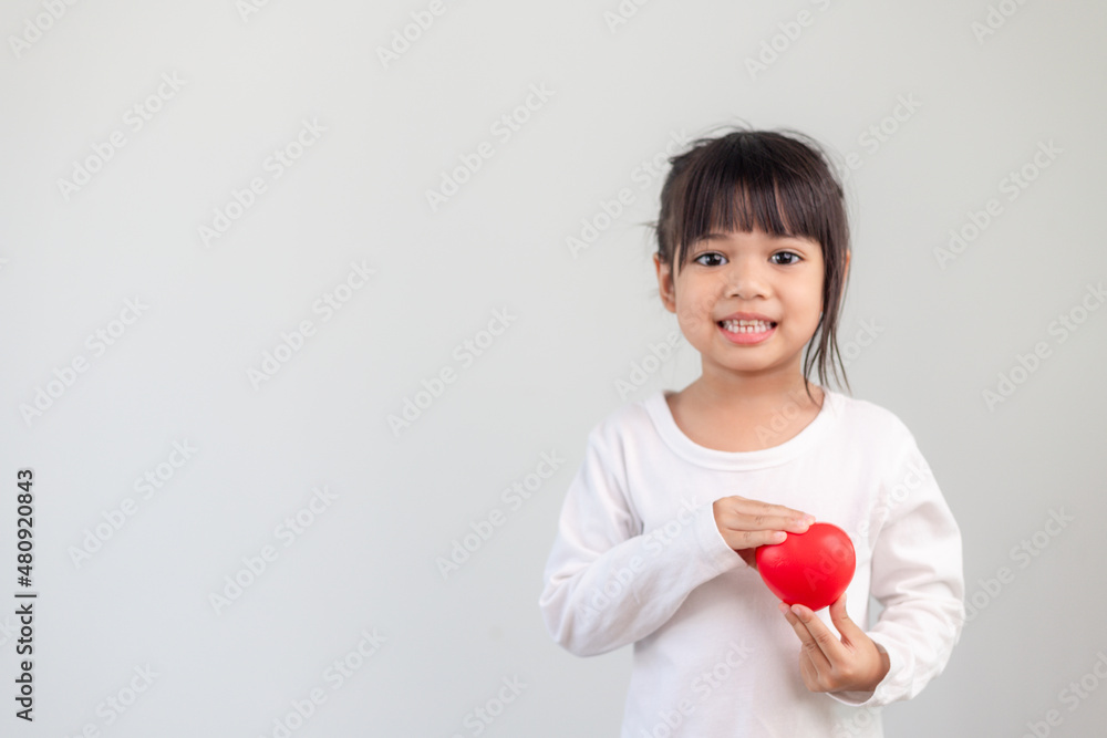 The little girl in a white shirt holding a red heart on a white background. Greeting cards for valentine's day, mother's day, father's day. The little girl in a white shirt holding a red heart on a white background. Greeting cards for valentine's day, mother's day, father's day.