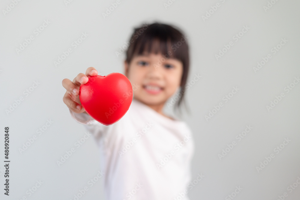 The little girl in a white shirt holding a red heart on a white background. Greeting cards for valentine's day, mother's day, father's day. The little girl in a white shirt holding a red heart on a white background. Greeting cards for valentine's day, mother's day, father's day.