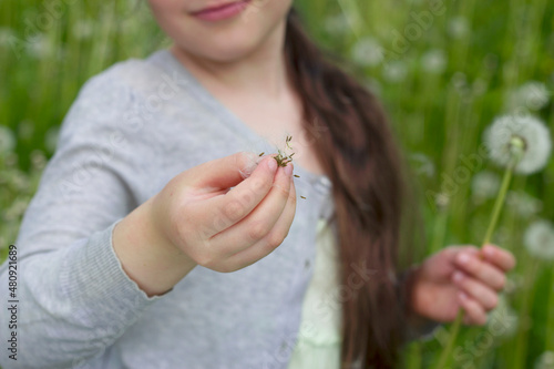 smiling girl with long dark hair with dandelion seeds in her hand