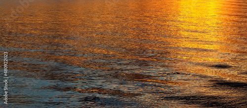 Gold water background during sunset or sunrise with waves and sunny reflection.