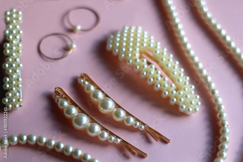 Various pearl jewelry and hair accessories on pink background. Selective focus.