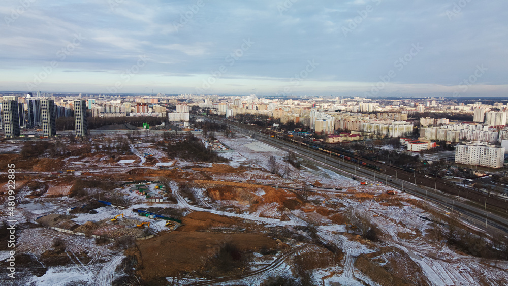 Construction site in a city vacant lot. Close to populated urban areas. Traces of heavy construction equipment are visible on the ground. Snow covered earth. Aerial photography.