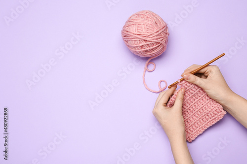 Woman crocheting with pink thread on violet background, top view. Space for text photo