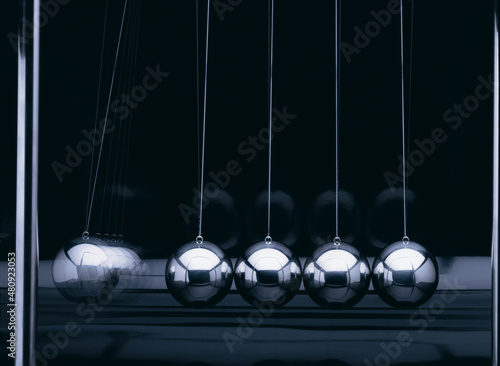 Newton-Pendel mit 5 silber-farbenen Kugeln in einer Reihe, seitlich fotografiert vor schwarzem Hintergrund