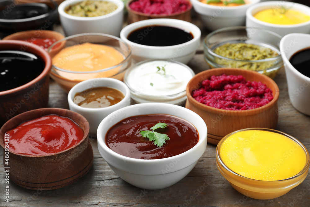 Many bowls with different sauces and herbs on wooden table Many bowls with different sauces and herbs on wooden table