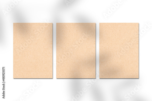 Three blank brown kraft paper cards, vertical A4 poster or business card mockup on a white background with leaf shadow. Flat lay, top view. For advertising, brand design, stationery presentation.