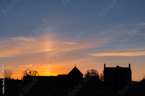Silhouette of a Catholic church and old building at sunset. Beautiful sky with sun glow and light beam over the roof of the church. Urban city scene. Warm and cool tone.