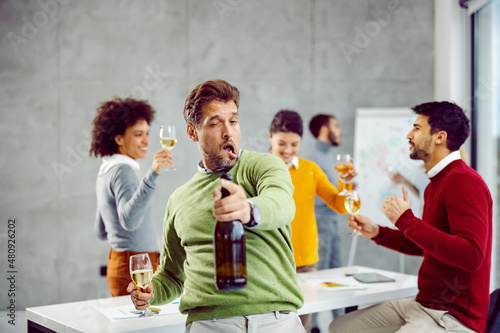 Drunk businessman celebrating at work. A drunk and tipsy businessman standing in his office and celebrating success while his colleagues having fun in the background. photo
