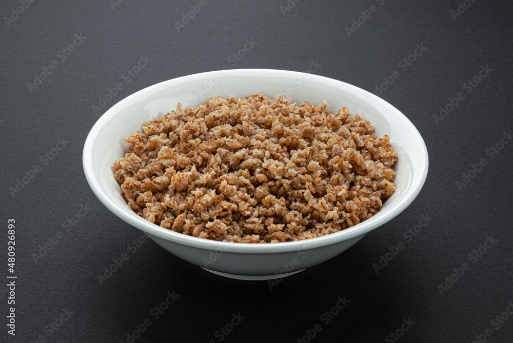 Bowl of buckwheat flakes on black background Bowl of buckwheat flakes on black background