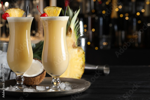 Tasty Pina Colada cocktails and ingredients on black wooden bar countertop, space for text