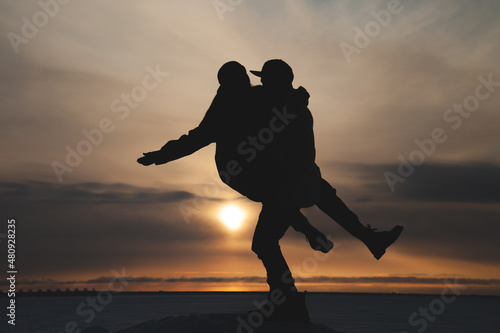 Silhouettes of a couple in love in winter against the background of the setting sun