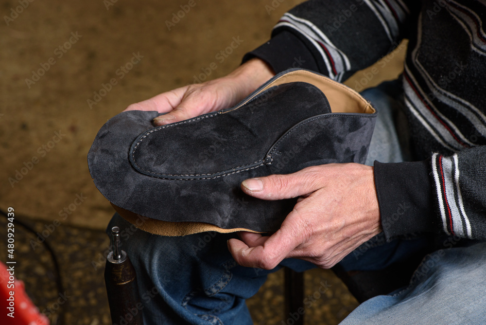 Bootmaker making shoes sitting in workshop. Shoemaker holding gray suede shoe in hands before stitching. Bespoke handmade shoes. Bootmaker making shoes sitting in workshop. Shoemaker holding gray suede shoe in hands before stitching. Bespoke handmade shoes.