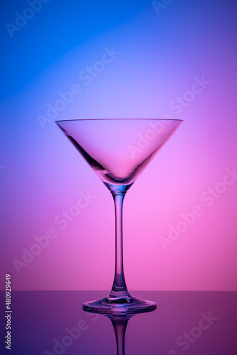 Empty martini glass on a pink and blue neon background. Alcohol drink, cocktail party concept. Transparent silhouette, illuminated effect. Night bar.