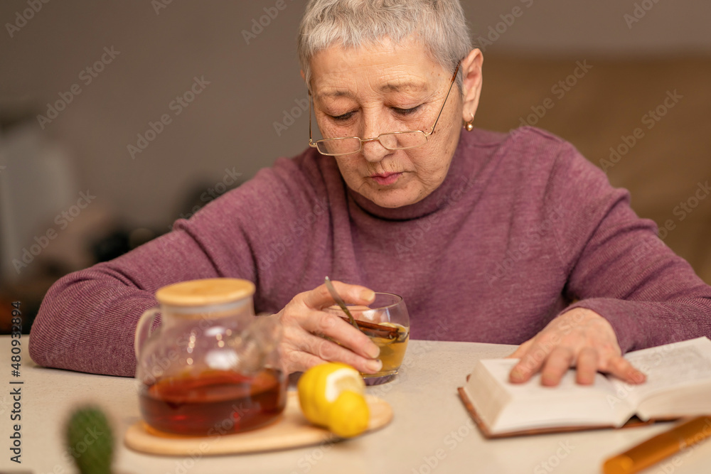woman sitting at the table drinking tea with lemon and reading a book woman sitting at the table drinking tea with lemon and reading a book