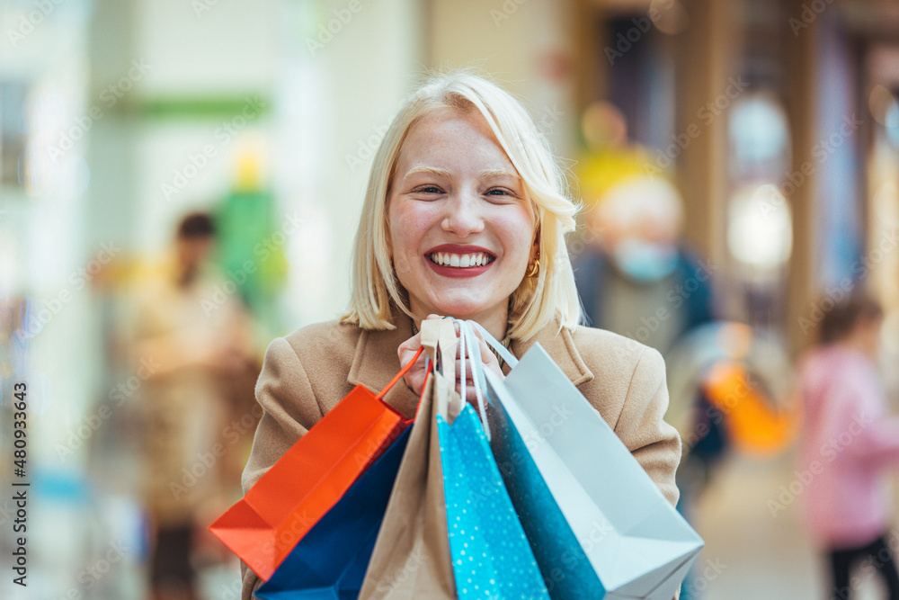 Happy young blond woman with shopping bags against a Shopping mall. Shopping woman holding shopping bags. Happiness, consumerism, sale and people concept Happy young blond woman with shopping bags against a Shopping mall. Shopping woman holding shopping bags. Happiness, consumerism, sale and people concept