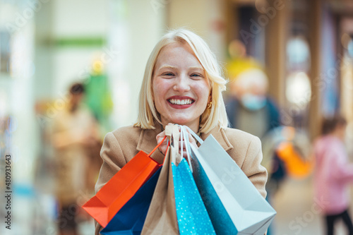 Happy young blond woman with shopping bags against a Shopping mall. Shopping woman holding shopping bags. Happiness, consumerism, sale and people concept