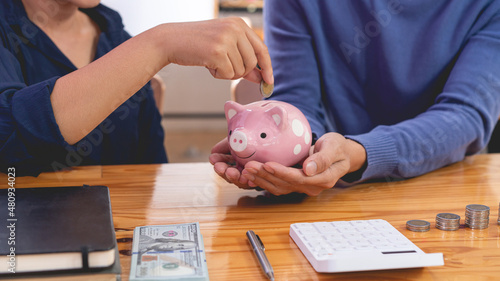 saving concept the female who wear long sleeved shirt trying to drop a coin into a pigging bank while the guy in lighter blue sweater carrying it for her photo