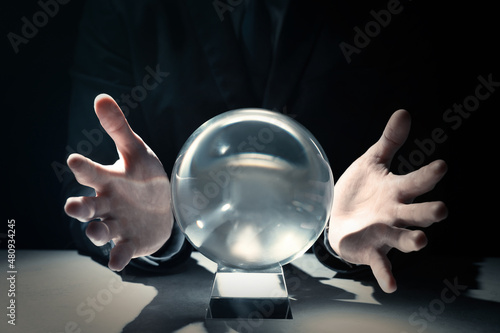 Businessman using crystal ball to predict future at table in darkness, closeup photo