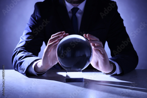 Businessman using crystal ball to predict future at table, closeup photo
