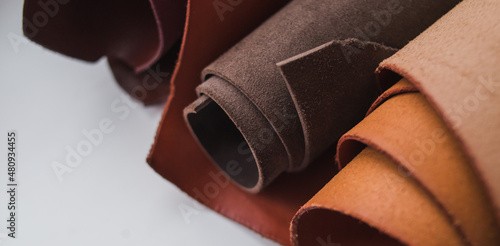 Rolls of genuine brown leather on a white background. Materials for leather goods. Manufacturing of leather goods. Banner
