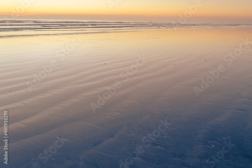 beach at sunset with linear formations in the sand with water with orange colors