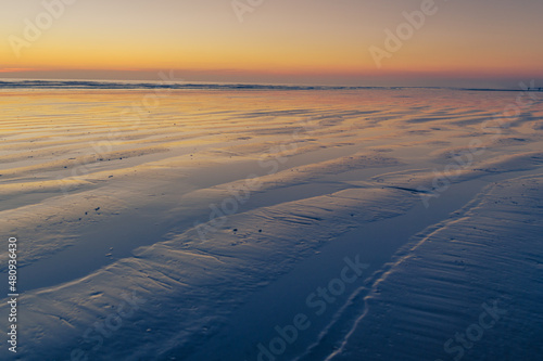 beach at sunset with linear formations in the sand with water with orange colors