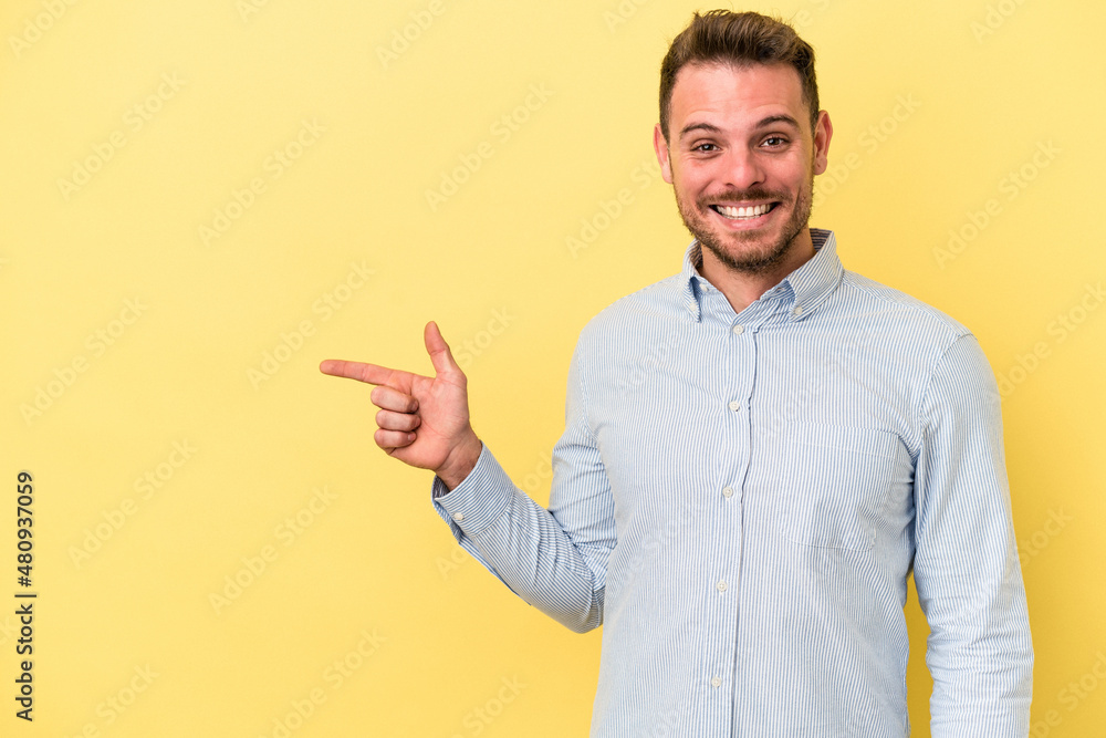 Young caucasian man isolated on yellow background smiling cheerfully pointing with forefinger away. Young caucasian man isolated on yellow background smiling cheerfully pointing with forefinger away.