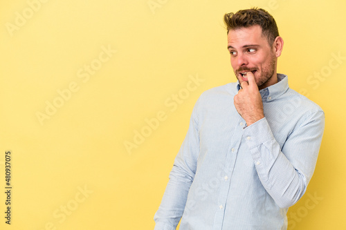 Young caucasian man isolated on yellow background relaxed thinking about something looking at a copy space.