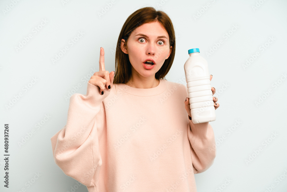 Young English woman holding a bottle of milk isolated on blue background having an idea, inspiration concept. Young English woman holding a bottle of milk isolated on blue background having an idea, inspiration concept.