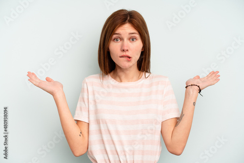 Young English woman isolated on blue background confused and doubtful shrugging shoulders to hold a copy space.