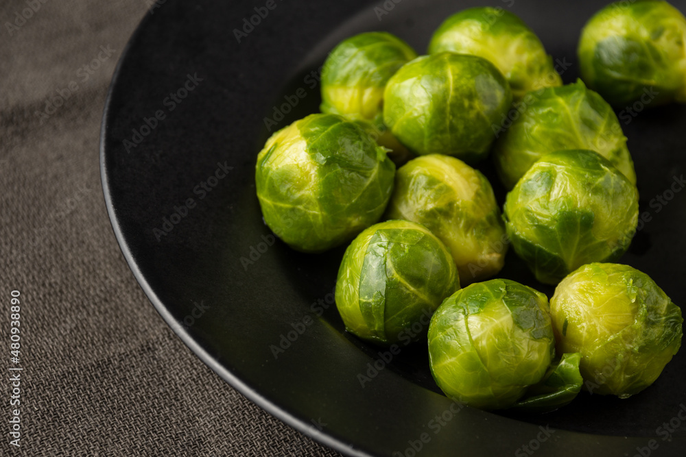 Top view of frozen brussels sprouts on black plate and dark cloth, selective focus, horizontal Top view of frozen brussels sprouts on black plate and dark cloth, selective focus, horizontal
