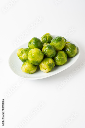 Top view of green Brussels sprouts on white plate, white background, vertical, with copy space
