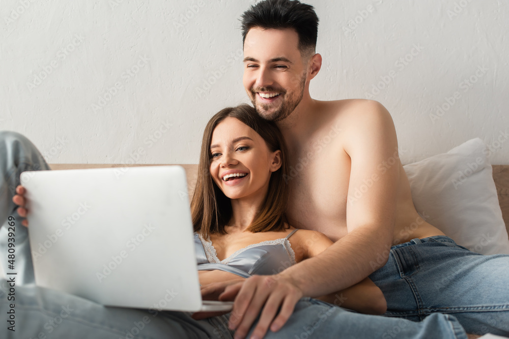 joyful couple of lovers watching comedy film on blurred laptop in bed.