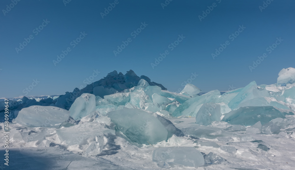 A block of turquoise ice hummocks on a frozen lake. Sun glare on the edges. Shadows on the snow. The background is a clear blue sky. Copy space. Close-up. Baikal