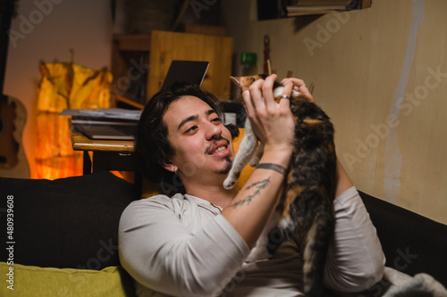 man laying on a sofa at home and playing with his cat