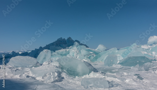 A block of turquoise ice hummocks on a frozen lake. Sun glare on the edges. Shadows on the snow. The background is a clear blue sky. Copy space. Close-up. Baikal