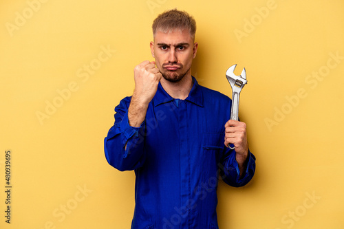 Young electrician caucasian man isolated on yellow background showing fist to camera, aggressive facial expression.
