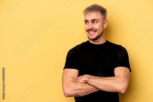 Young caucasian man isolated on yellow background smiling confident with crossed arms.