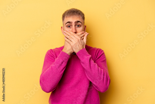 Young caucasian man isolated on yellow background covering mouth with hands looking worried.