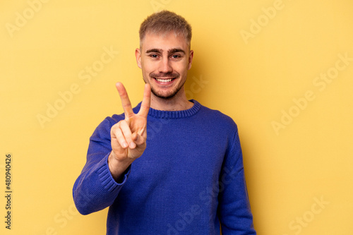 Young caucasian man isolated on yellow background showing victory sign and smiling broadly.