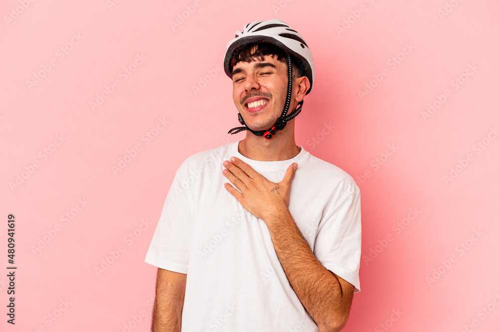 Young mixed race man wearing a helmet bike isolated on pink background laughs out loudly keeping hand on chest. Young mixed race man wearing a helmet bike isolated on pink background laughs out loudly keeping hand on chest.