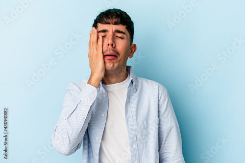 Young mixed race man isolated on blue background tired and very sleepy keeping hand on head.