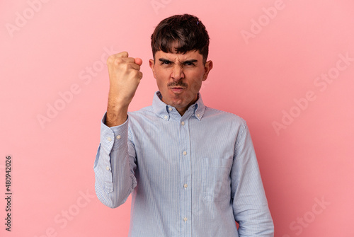 Young mixed race man isolated on pink background showing fist to camera, aggressive facial expression.