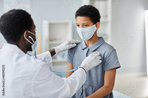 Doctor using stethoscope while checking breathing of teenage girl during medical exam in pediatric clinic, copy space