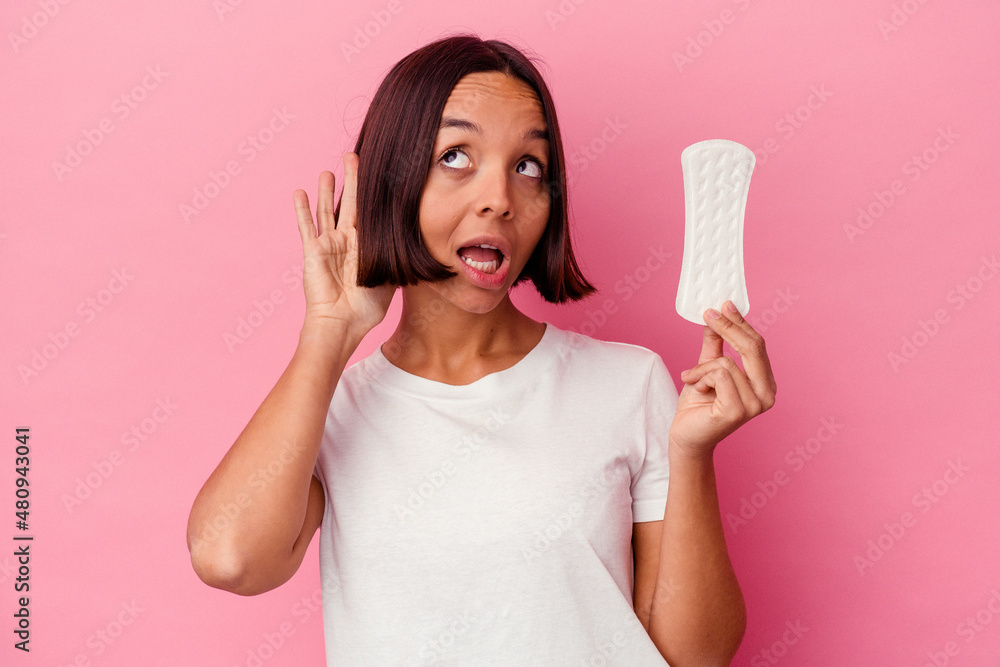 Young mixed race woman holding a compress isolated on pink background trying to listening a gossip. Young mixed race woman holding a compress isolated on pink background trying to listening a gossip.