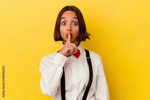 Young mixed race waitress woman isolated on yellow background keeping a secret or asking for silence. photo