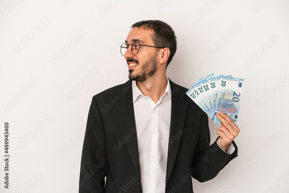 Young caucasian business man holding banknotes isolated on white background looks aside smiling, cheerful and pleasant. Young caucasian business man holding banknotes isolated on white background looks aside smiling, cheerful and pleasant.